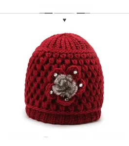 Detail of red cable-knit winter hat featuring crochet flower with faux fur ball and rhinestones