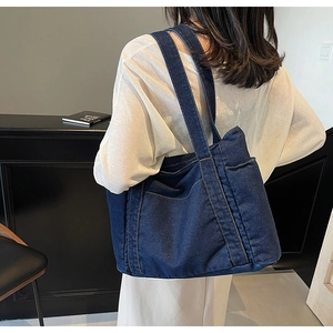 Side view of large dark blue denim tote bag worn by a model in casual white outfit