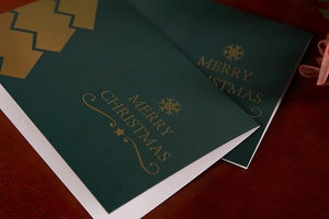 Close-up of luxury green Christmas cards with gold foil lettering on a wooden desk