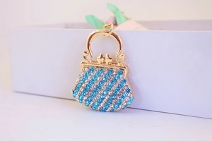 Detailed macro of a gold handbag charm featuring blue and white rhinestones and a top loop