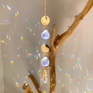Close-up of golden sun catcher with crystal prisms hanging from a branch creating rainbows