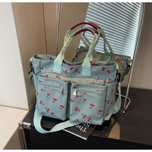 Detail of light green cherry print tote bag with red handles and multiple pockets