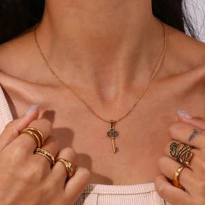 Close-up of golden key pendant necklace with green gemstone and snake-shaped rings