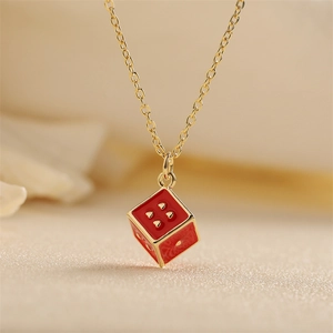 Collana dorata con ciondolo a dado in smalto rosso e punti dorati su sfondo beige
