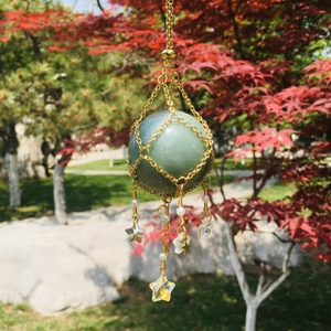 Close-up of green crystal orb encased in a gold mesh net with star and pearl charms