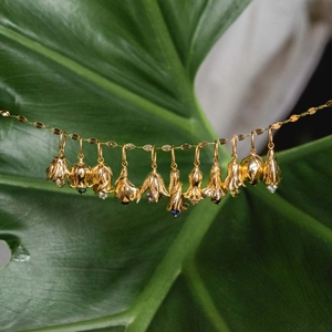 Gold flower bud necklace with birthstones hanging elegantly over green leaves