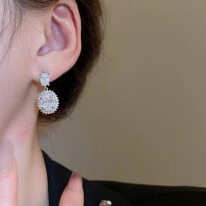 Close-up of elegant silver earrings with zircon pendants worn on a female ear model