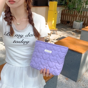 Outdoor shot of a purple quilted heart cosmetic bag held by a model in casual outfit
