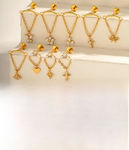 Macro detail of gold-plated titanium bow and heart cartilage studs with chains and zircons