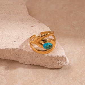 Gros plan sur une bague spirale dorée avec zircon bleu ovale sur fond de pierre brute