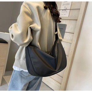 Minimalist black dumpling crossbody bag with satiny finish worn by a model in a modern room