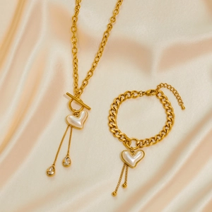 Exaggerated gold heart pearl necklace and bracelet set on elegant champagne silk fabric