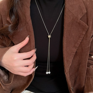 Détail du collier lariat doré ajustable avec fermoir en zircon et perles sur une veste chic