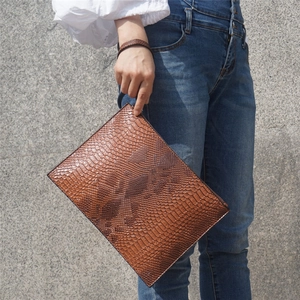 Close-up of brown python-patterned PU leather envelope bag held against a stone wall