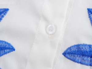 Close-up of blue leaf embroidery and white button detail on vacation style resort top