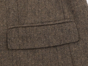 Dettaglio del blazer in tweed a spina di pesce marrone con trama del tessuto e tasca