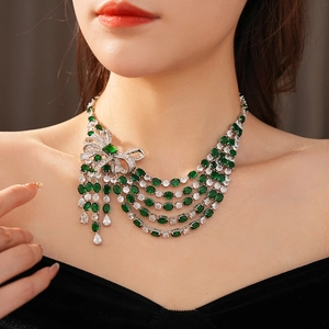Gros plan détaillé d'un collier multicouche avec pierres vertes et pompon nœud en zircon