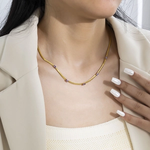 Detail showing gold blade chain necklace with rectangular purple zircon stones on a model