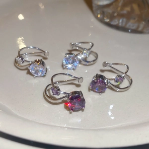 Detailed view of silver zircon ear cuffs in purple and white on a ceramic tray