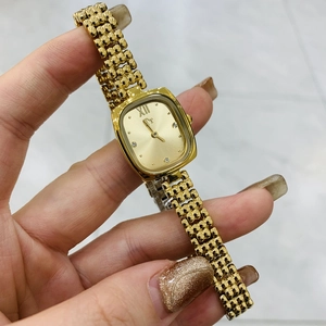 Macro detail of golden square watch dial with rhinestones and metal chain bracelet