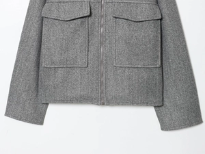 Détail d'une veste en laine grise avec de grandes poches à rabat et fermeture éclair en métal