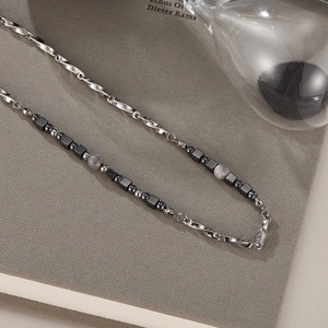 Detail of beaded titanium steel necklace with black hematite and silver chain on grey book