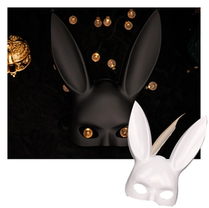 Artistic display of black matte and white glossy bunny party masks with warm ambient lighting