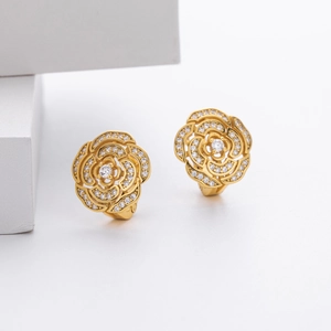 Macro detail of golden camellia flower earrings with cubic zirconia and metal texture