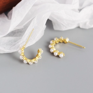 Macro shot of gold C-shaped hoop earrings with embedded pearls on a neutral background