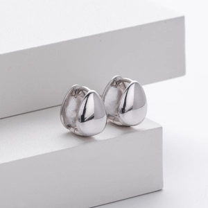 Macro detail of silver teardrop earrings on white stone displaying polished finish