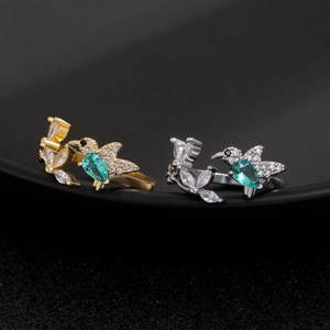Macro detail of hummingbird ring with green gemstone and pave crystals in gold and silver