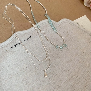 Close-up of double-layer silver water drop necklace and blue beaded chain on linen