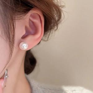 Close-up of elegant white round pearl stud earrings worn by a model in soft lighting