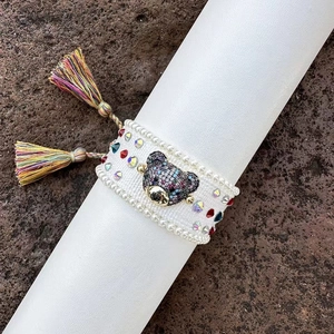 Detail of hand-woven bracelet with colorful rhinestones, pearl trim and a bear charm