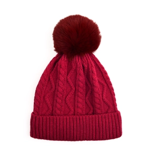 Macro detail of wine red cable knit texture and faux fur pom-pom on winter hat