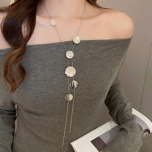 Détail d'un collier multicouche argenté avec des pendentifs circulaires sur un pull gris