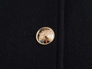 Detailed close-up of an embossed gold crest button on a premium black wool short coat