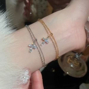 Close-up of gold and silver cross charm bracelets with zircon inlays and fine bead chains