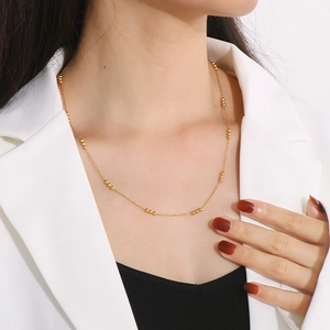 Minimalist gold beaded stainless steel necklace worn by a model in a white blazer