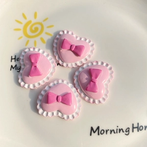 Detailed macro view of four pink heart resin charms with 3D bows and scalloped white edges