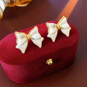 Détail de boucles d'oreilles nœud plaquées or 14K avec émail crème sur écrin de velours