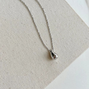 Close-up of minimalist silver bean pendant necklace on textured beige fabric