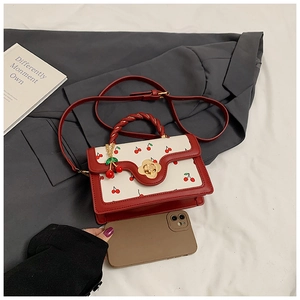 Detail of red cherry print mini crossbody bag with gold floral clasp on a suit background