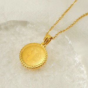 Golden Saint Benedict medal round pendant necklace with fine chain on textured background