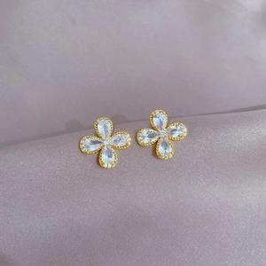 Detailed close-up of golden clover earrings with sparkling clear zircon on purple silk fabric