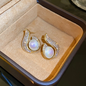 Macro shot of gold-plated fishtail earrings with iridescent pearls and zircon stones
