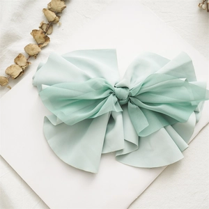 Detail of a mint green fabric bow hair clip with layered tulle on a white card