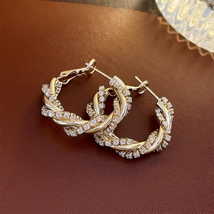 Close-up of twisted golden hoop earrings with clear crystals on a textured leather surface