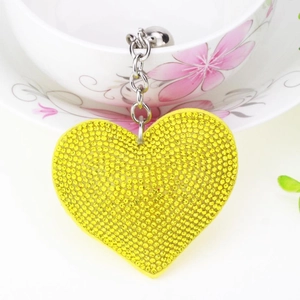 Detail of yellow rhinestone heart keychain with metal chain on a floral teacup edge