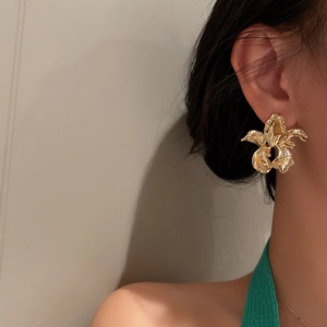 Macro detail of irregular golden flower earrings with textured metallic petals on model